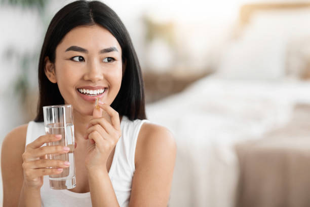 Diet, nutrition, healthy eating concept. Close Up Of Happy Smiling Asian Woman Taking Supplement Pill And Holding Glass Of Fresh Water In Morning, copy space|||