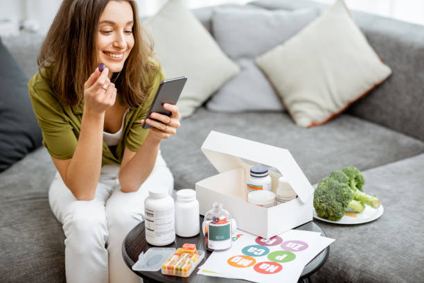Woman taking nutritional supplements in the form of pills while sitting with smart phone at home. Concept of individual online selection of food supplements. Preventive medicine||||