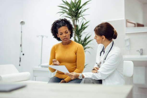 Female patient and doctor discussing test results in medical office.||Senior black woman sits on the couch at home and takes medications from a daily pill organizer. Cropped shot does not show the woman's face.|