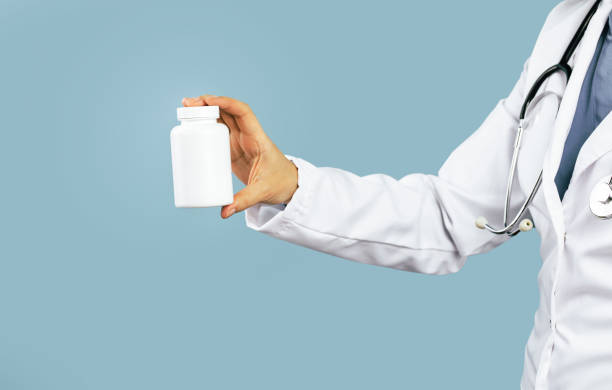 Hand of female doctor mid-section holds white pills or tablets jar mockup. Medicine and pharmacy, prescription drugs or vitamins concept. Copy space banner|Supplements and vitamins on a white background. Selective focus. Medicine.||